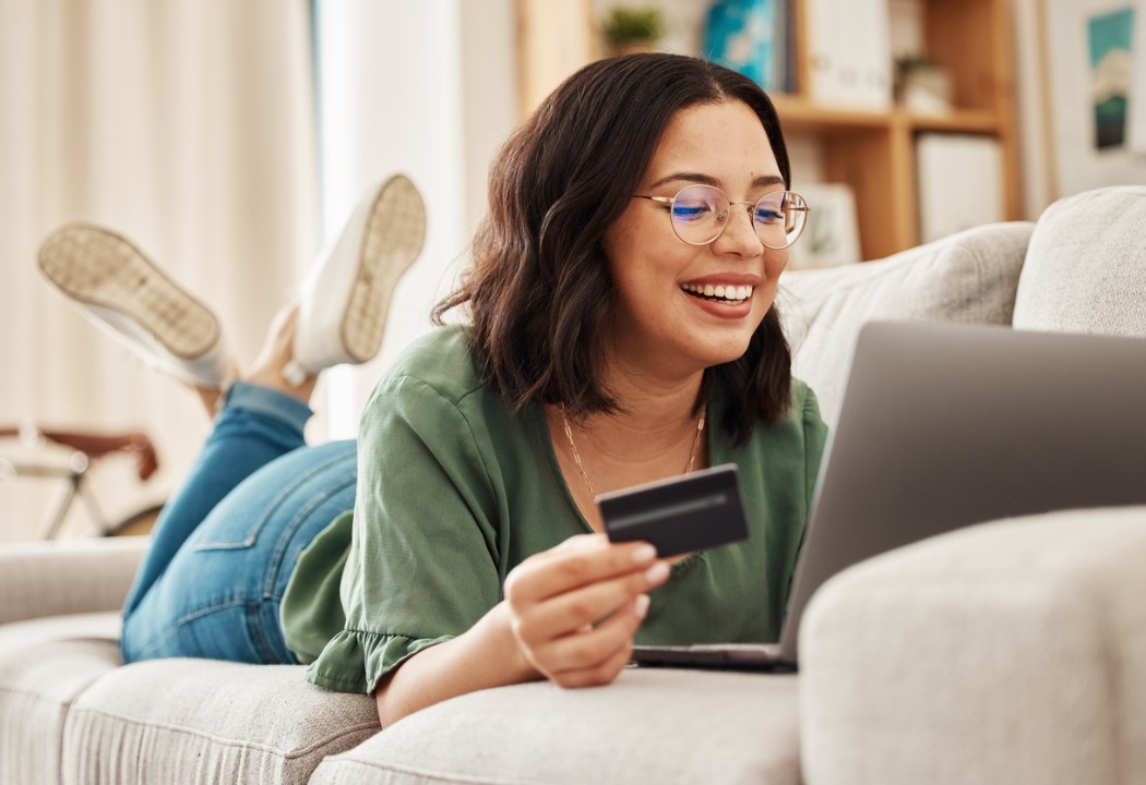 Woman on couch holding credit card looking at laptop